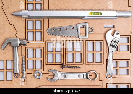 Miniaturkopien von wichtigen Handwerkzeugen und Befestigungselementen, die auf einem Rahmen des Flachbau-Modellbausatzes angeordnet sind. Home Engineering und Bau Hintergrund. Stockfoto