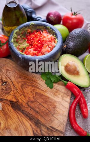 Making Guacamole - zerdrückte Avocado in Marmormörtel und Zutaten Stockfoto