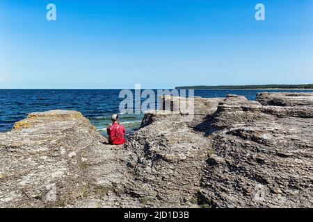 Wanderer, der zwischen Kalksteinsäulen sitzt und auf das Meer blickt, Raukar am Ufer von Kalmarsund, Byrum, Westküste der Insel Oeland, Kalmar Stockfoto