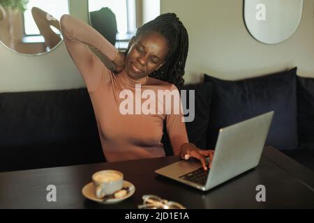 Ängstlich und müde gemischte Rasse Geschäftsfrau, Hals halten, Schmerzen fühlen, mit Laptop im Café. Sitzende Arbeit, falsche Haltung Stockfoto