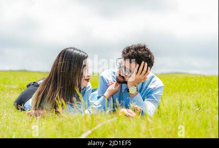 Zwei verliebte Menschen liegen auf dem Gras und schauen sich an, Ein Paar liegt auf dem Gras und schaut sich an, Junges Paar verliebt liegt auf dem Stockfoto