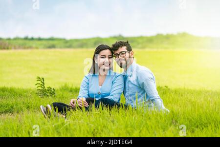 Junges verliebtes Paar sitzt auf dem Gras und schaut auf die Kamera, zwei Liebende sitzen auf dem Gras und schauen auf die Kamera, Porträt eines verliebten Paares Stockfoto