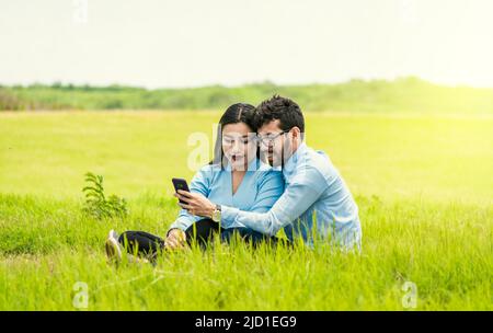 Junges verliebter Paare, die ein Selfie auf dem Feld machen, zwei Liebhaber, die auf dem Gras sitzen und Selfies machen, verliebte Menschen, die Selfies auf dem Feld machen Stockfoto