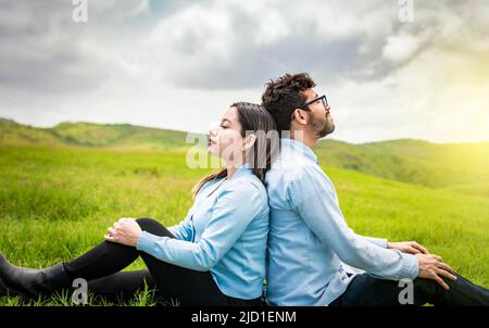 Ein Paar sitzt mit dem Rücken zueinander auf dem Gras, Hochzeitspaar auf dem Feld sitzt mit dem Rücken zueinander in Richtung der schauen Stockfoto