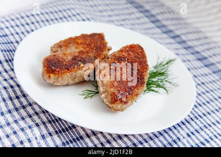 Weißer Teller mit Rinderschnitzel auf traditionellem Küchentuch mit Schachbrettmuster Stockfoto