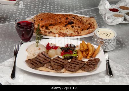 Shish Kebab wird aus Lamm hergestellt. Auf dem Esstisch stehen Shish Kebab, Pita-Brot und Fruchtsaft. Lammkoteletts. Stockfoto