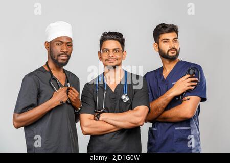 Attraktives medizinisches Team, das auf hellgrauem Hintergrund zusammensteht. Afroamerikanische Krankenschwester und zwei indische Ärzte Stockfoto