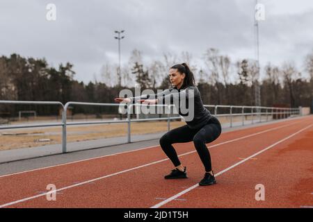 Frau macht Kniebeugen auf Laufstrecke Stockfoto
