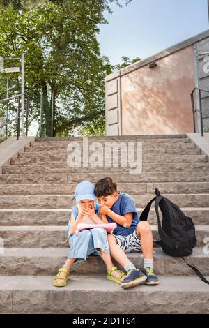 Kinder, die auf Treppen sitzen und ein Tablet benutzen Stockfoto