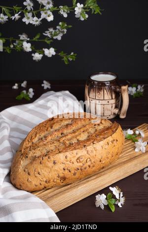 Frisches hausgemachtes Roggen-Getreidebrot mit Tonkrug Milch auf Holzschneidebrett. Gesundes Frühstück Stockfoto