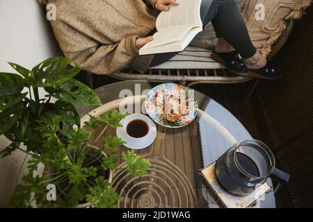 Frau liest Buch und trinkt Tee und Snack Stockfoto