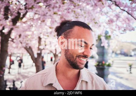 Lächelnder junger Mann, der unter der Kirschblüte steht Stockfoto