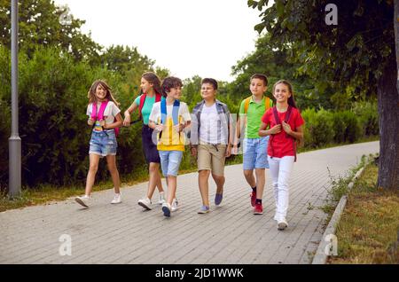 Lustige Schulkinder Gruppe mit Rucksäcken haben Spaß zusammen auf dem Weg im Park zu gehen. Stockfoto