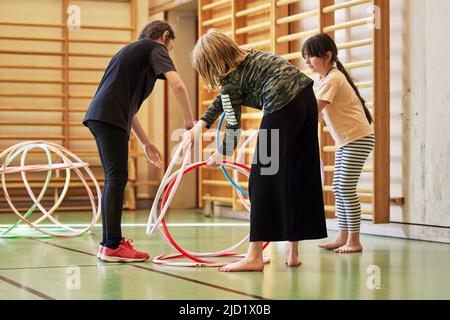 Kinder spielen mit Hula Hoop Reifen in der Schulhalle Stockfoto