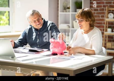 Junger Mann, Blick auf Frau einfügen Münze im Sparschwein Stockfoto