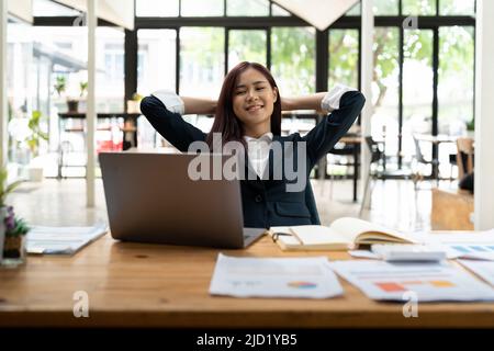 Junge asiatische Geschäftsfrau mit Pause und Ruhe nach der Lösung der Aufgabe im modernen Büro. Stockfoto