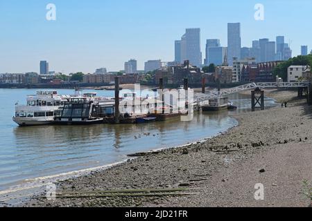 London, Großbritannien. An einem Anlegesteg in Bermondsey vertäuten Ausflugsboote auf der Themse. Ebbe offenbart das Vorland. Türme von Canary Wharf im Hintergrund. Stockfoto