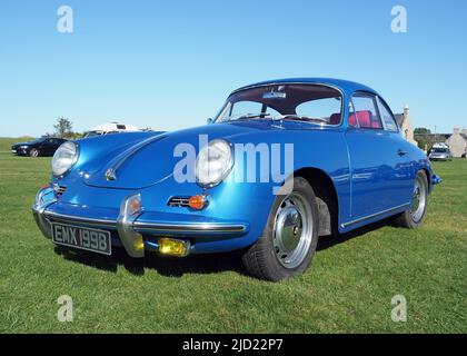 Seitenansicht eines Porsche-Coupés vom Typ C des Typs 356 aus dem Jahr 1964 in Metallic-Blau mit 1,6lt Motoren. Heller, sonniger Tag mit blauem Himmel bei einer Autoschau auf Rasenspielfeldern. Stockfoto