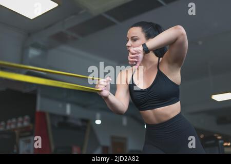 Junge sportliche kaukasische Frau ruft mit Smartwatch während des Trainings mit Gummiband Stockfoto