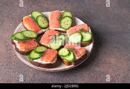 Sandwiches mit gesalzenem Lachs, Gurken und Dill auf weißem Brot auf braunem Hintergrund Stockfoto