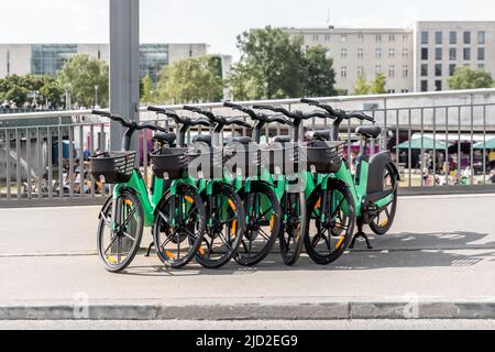 Viele moderne grüne E-Bikes teilen sich auf der Stadtstraße geparkt. Selbstbedienungsverleih für Straßentransport. Mieten Sie ein urbane Mobilität Fahrzeug mit Stockfoto