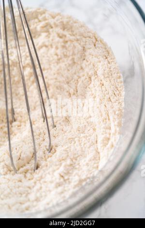 Zitronenkeks mit weißer Schokolade. Mischen Sie trockene Zutaten mit einem Handbesen in einer großen Glasschüssel, um Zitronenplätzchen mit weißer Schokolade zu backen. Stockfoto