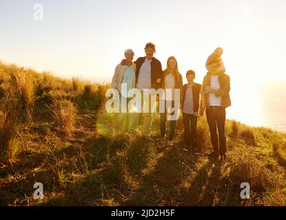 Sie sind am glücklichsten, wenn sie alle zusammen sind. Ein Porträt einer glücklichen Familie, die bei Sonnenuntergang auf einem grasbewachsenen Hügel steht. Stockfoto