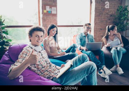 Foto von selbstbewussten positiven Gruppenmitgliedern, die im Schlafsaal sitzen und Prüfungen vorbereiten, die Themen in der Workstation-Werkstatt studieren Stockfoto