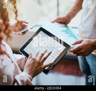 Die Berechnungen wurden durchgeführt. Aufnahme von zwei Händen, die nicht erkennbar waren und auf einem Tablet arbeiteten und sich die Geschäftscharts im Büro angeschaut haben. Stockfoto