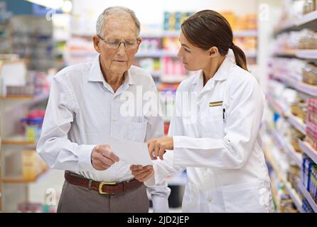 Ihre Kunden auf dem Laufenden halten. Aufnahme eines jungen Apothekers, der einem älteren Kunden mit seinem Rezept hilft. Stockfoto