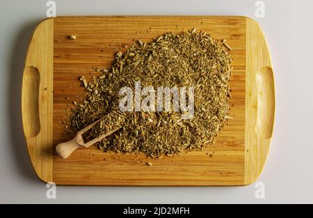 Trockene Mate-Blätter, traditionelles Getränk aus Argentinien, auf einem Holzbrett und einem Holzlöffelspender. Hintergrund und Textur von trockenem Tee. Stockfoto