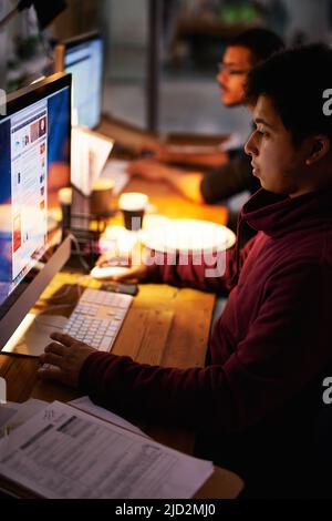 Die Arbeit erledigen. Eine kleine Aufnahme einer Gruppe junger Mitarbeiter, die in einem schwach beleuchteten Büro arbeiten. Stockfoto