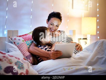 Es ist Zeit für ein anderes.... Aufnahme einer attraktiven jungen Schwangeren, die ihre Tochter auf einem Tablet mit einer Geschichte zur Schlafenszeit vorliest. Stockfoto