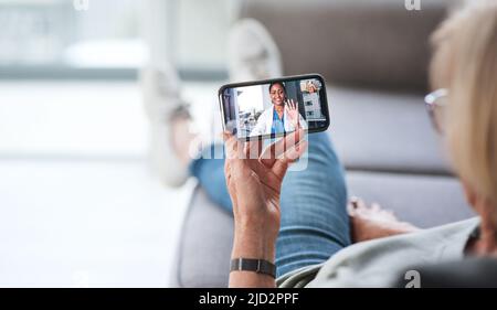 Die bequemste Beratung aller Zeiten. Aufnahme einer älteren Frau, die ein Smartphone benutzt, um einen Videoanruf mit ihrem Arzt auf dem Sofa zu Hause zu tätigen. Stockfoto