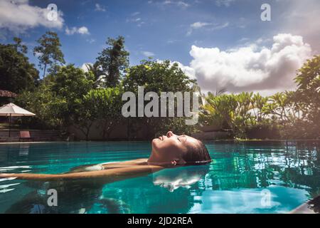 Frau im Pool Wasser entspannen. Eine schöne Frau, die im Wasser in einem Schwimmbad schwimmt. Entspannung und Ruhe. Augen geschlossen und Wellness-Genuss in Stockfoto