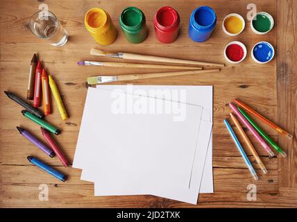 Kreativität geht nie aus dem Stil. Leeres weißes Papier mit Malutensilien und Bleistiften auf einem Holztisch. Stockfoto