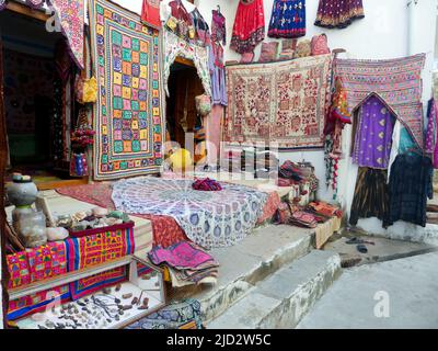 Pushkar, Rajasthan Indien - 4. November 2019 : lokaler Straßenmarkt verkauft Teppiche, Teppiche, Kleidungsstücke hängen außerhalb Shop Stockfoto