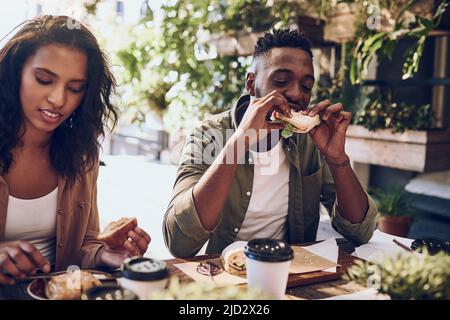 Zu einem guten Sandwich kann ich gar nicht nein sagen. Eine kleine Aufnahme eines glücklichen jungen Paares zum Mittagessen in einem Café. Stockfoto