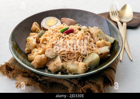 Gebratene Instantnudeln mit grünem, mit Huhn (Kaeng Khiao wan) und gekochtem Ei in süßer, brauner Sauce in einer Keramikschale mit Besteck-Set verrühren Stockfoto