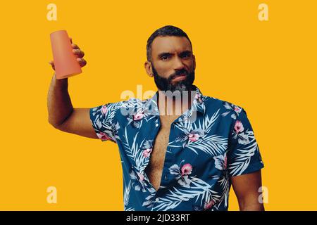 Glücklicher afroamerikanischer Mann, der ein hawaiiianisches Hemd trägt und ein leeres Cocktailglas im Studio aufgenommen hat Stockfoto