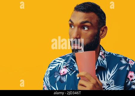 Glücklicher afroamerikanischer Mann, der ein hawaiianisches Hemd mit einem Cocktail-Glas und einer Strohaufnahme im Studio trägt Stockfoto