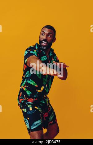 Schöner bärtiger afroamerikanischer Mann mit mittlerem Erwachsenen, der lächelt und tanzt, in hawaiianischen Shorts und Hemd auf der Aufnahme im Ferienstudio Stockfoto