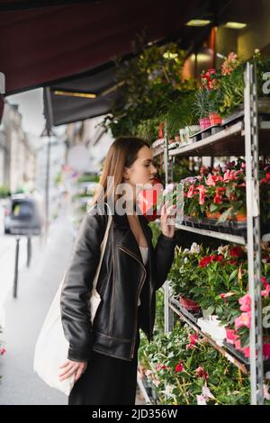 Seitenansicht einer stilvollen Frau mit Einkaufstasche aus Canvas mit Blick auf grüne Topfpflanzen auf der Straße in paris Stockfoto