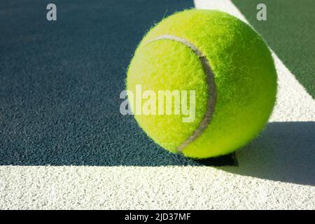 Nahaufnahme eines Tennisballs, der an einem sonnigen Tag in einer gemalten Linie auf einem Hartplatz sitzt Stockfoto