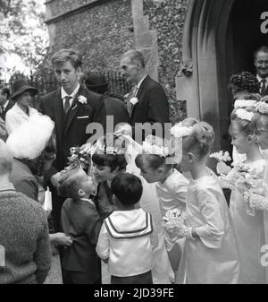 1960s, historisch, vor einem Kircheneingang, eine gerade verheiratete Braut, umgeben von ihren jungen Brautjungfern, die einen Kuss von einem Page Boy, England, Großbritannien, bekommen. Stockfoto