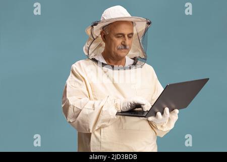 Reifer Bienenhalter in Uniform mit einem Laptop-Computer auf blauem Hintergrund isoliert Stockfoto