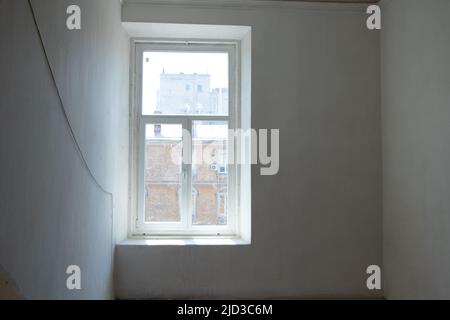 Ein Fenster mit Blick auf die Fassade eines Hauses an einer weißen Wand in der Ecke in der Ukraine, ein Gebäude und ein Fenster an einer leeren Wand Stockfoto
