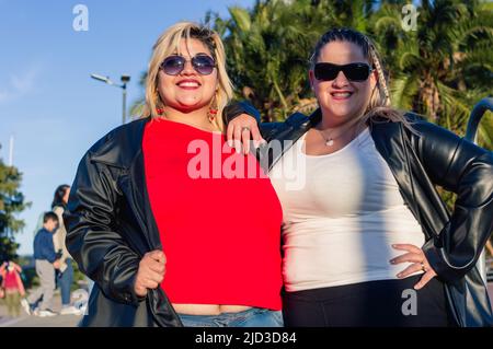 Zwei schöne mollige frauen aus dem lateinischen Kaukasus, die vor der Kamera posieren und die Kamera anblicken, mit Sonnenbrillen und legerer Kleidung lächeln, leben Stockfoto