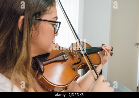 Seitenansicht junge lateinische kaukasische venezolanerin, die Geige spielt und zu Hause klassische Musik praktiziert. Nahaufnahme mit Kopierraum. Stockfoto