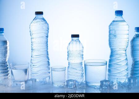 Verschiedene Arten von Eis-Mineralwasser-Flasche mit Gläsern Wasser auf blauem Hintergrund. Stockfoto